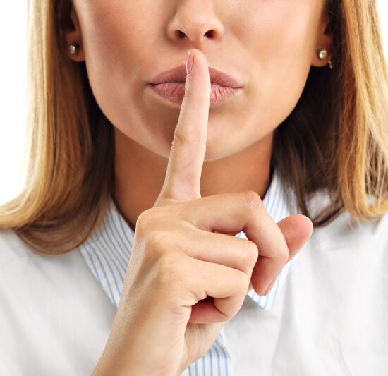 Woman in a white top placing her pointer finger to her lips to show a silence gesture