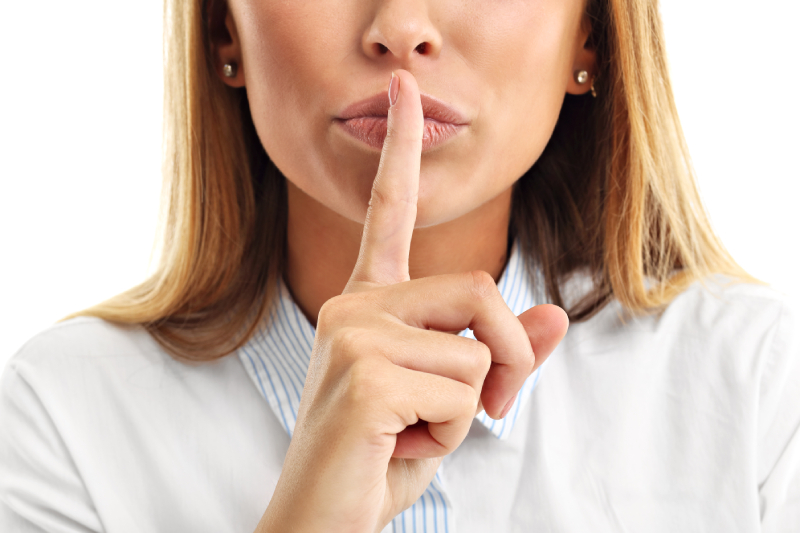 Woman in a white top placing her pointer finger to her lips to show a silence gesture