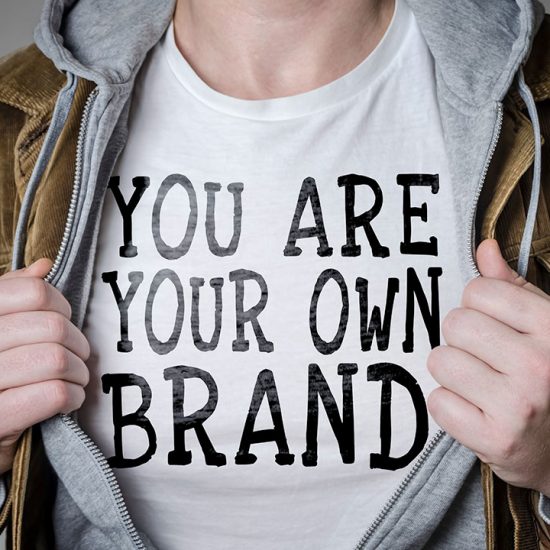 A person spreading open their jacket layers to reveal a white shirt that says “You are your own brand.”