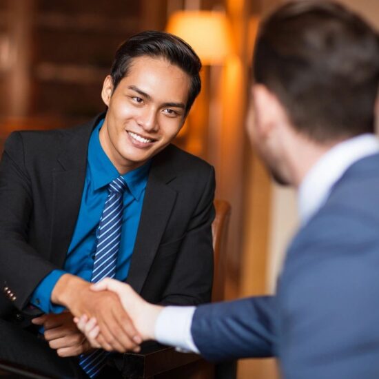 A brown-skinned man in a business suit shaking the hands of a white man in a blue business suit