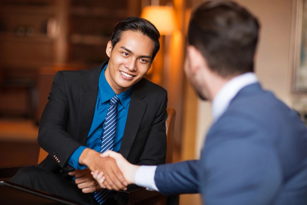 A brown-skinned man in a business suit shaking the hands of a white man in a blue business suit